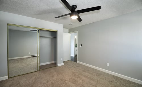 an empty living room with a ceiling fan and a mirrored closet at The Dexter Apartments in Denver, CO, 80246