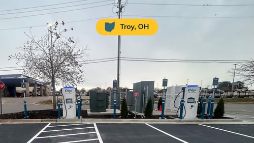 Several EVgo fast-charging units installed in marked parking spaces at a public charging station, with EVgo logos on the chargers, protective bollards around each unit