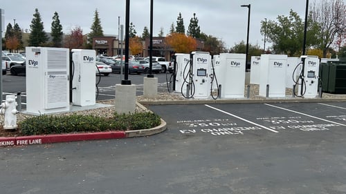 Several EVgo fast-charging units installed in marked parking spaces at a public charging station, with EVgo logos on the chargers, protective bollards around each unit