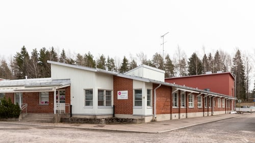 Juniori-Ainon sisäänkäyntiä ja rakennuksen julkisivua. Rakennus on yksikerroksinen punaisen ja valkoisen sävyinen tiilitalo.