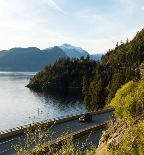 A car driving along The Sea-to-Sky Highway with mountains in the background.