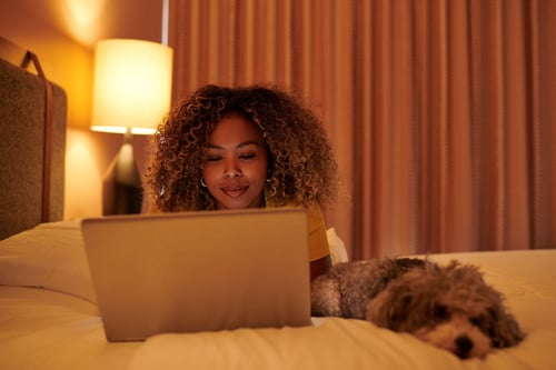 Women laying in bed with laptop next to her dog using Wi-Fi