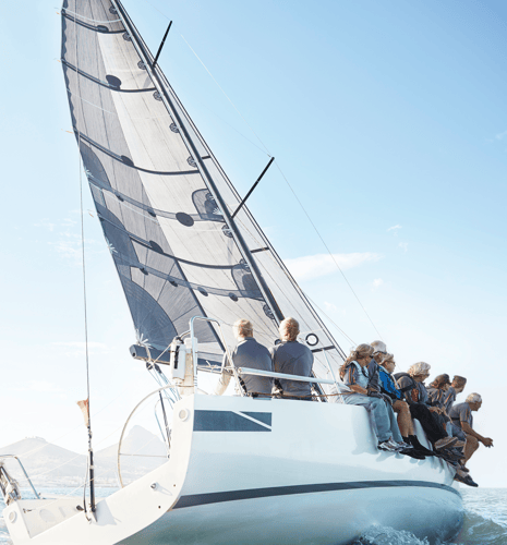 A group of people sitting on a sailboat, with a clear blue sky in the background.