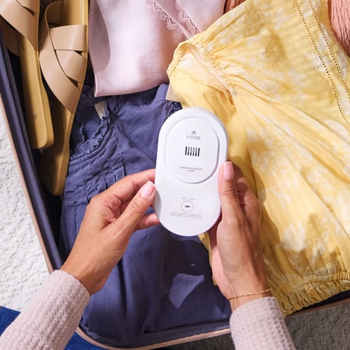 A person holds a CO alarm over their clothes in a suitcase.