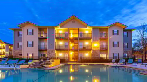 apartments at dusk with lights on behind swimming pool