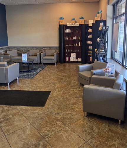 Lobby seating area at Hand & Stone Plymouth MI with gray chairs, product display shelves, and soft natural lighting.