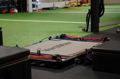 Grey machine with red and blue bands attached to it in front of green turf