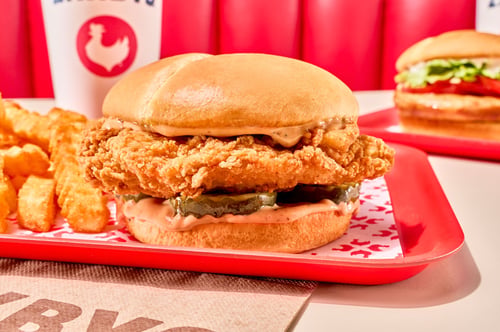 Zaxbys fried chicken signature chicken sandwich served with crinkle fries and a drink, with a grilled chicken sandwich in the background.
