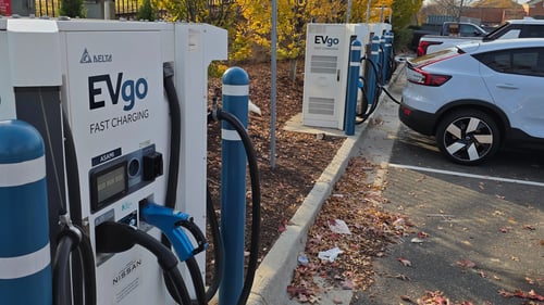 Several EVgo fast-charging units installed in marked parking spaces at a public charging station, with EVgo logos on the chargers, protective bollards around each unit