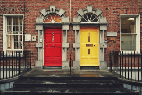 A brick townhouse with one red door and one yellow door.