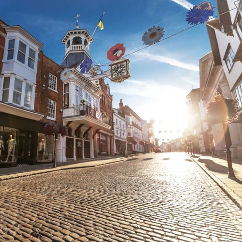 Knight Frank Guildford Estate Agents historic cobbled high street in Guildford England featuring the ornate guildhall clock and traditional timber-framed buildings under a bright morning sky