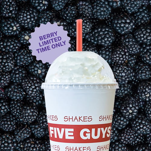 A Five Guys blackberry milkshake in a branded cup with a red straw and whipped cream, set against a background of fresh blackberries. A purple starburst badge reads “Berry Limited Time Only.”