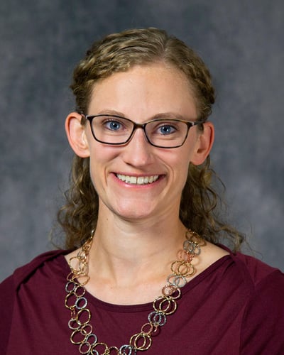 Tara is smiling at the camera in front of a gray background wearing a maroon shirt.
