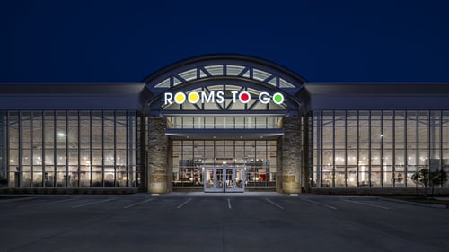 Rooms To Go furniture store facade illuminated at night in Pearland, TX, showcasing large glass windows and modern architecture.