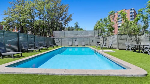 swimming pool with lounge chairs and green turf surrounding it backyard