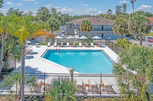 A pool surrounded by palm trees and chairs. at The Teale Golden Gate in Naples, FL, 34116