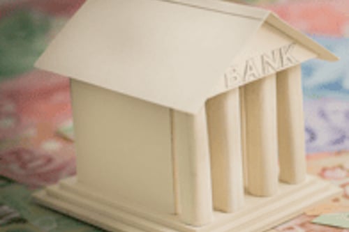 A model bank sitting atop a pile of Canadian paper currency in various denominations.