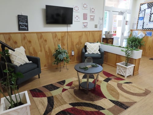 Bright and welcoming lobby with chairs for parents and a colorful bulletin board displaying cute moments from the daycare.