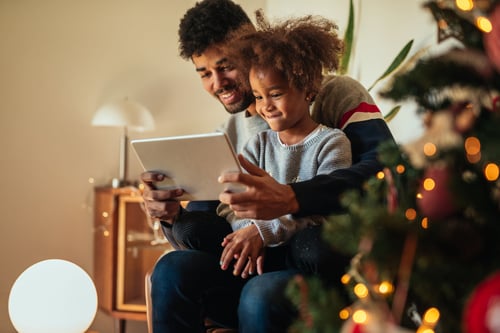 Dad and daughters sitting next to a Christmas Tree.
