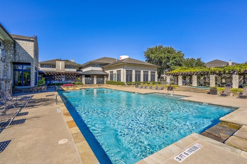 Beautiful swimming pool with tree lined view and lounge chairs at Cypress Lake at Stonebriar Apartments, Frisco, TX