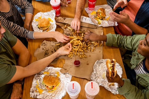 A top-down photograph of a group of friends enjoying a meal at a Five Guys restaurant.