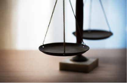 A close-up of a balanced scale on a wooden table, symbolizing justice and equality. The background is softly blurred, creating a calm, contemplative mood.