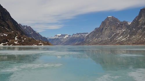 serene mountain range behind a still body of water, reflecting the mountains and the sky with scattered clouds
