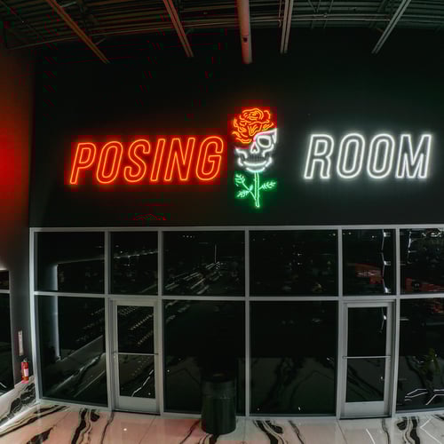 Neon-lit posing room with skull and rose sign at Absolute Recomp Las Colinas, representing the best hardcore strength training in Irving, TX.