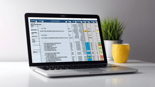 A laptop opened on a desk, showing a spreadsheet on the screen.