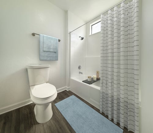 A white toilet in a bathroom with a blue rug at Charlmont Village Apartments in Ontario