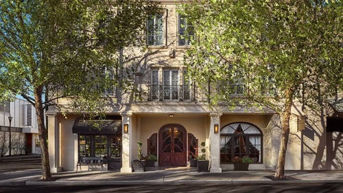 Two trees in front of a beige building with rectangular windows, decorative trim, and recessed first floor.