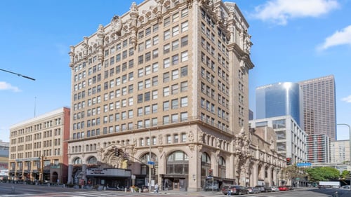 A large, ornate building with many windows sits in the middle of a city street at Grand Central Market Apartments, Los Angeles, CA, 90013