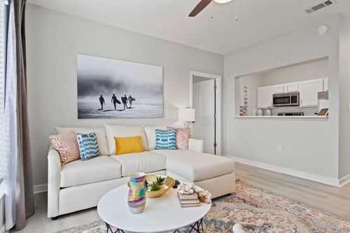 A living room with a white couch and a painting of three people walking on a beach at Elan Apartments in Fort Walton Beach, FL