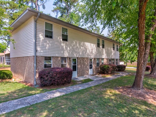 A small building with a white door and windows surrounded by greenery at Woodlocke Apartments, Moncks Corner, SC, 27461