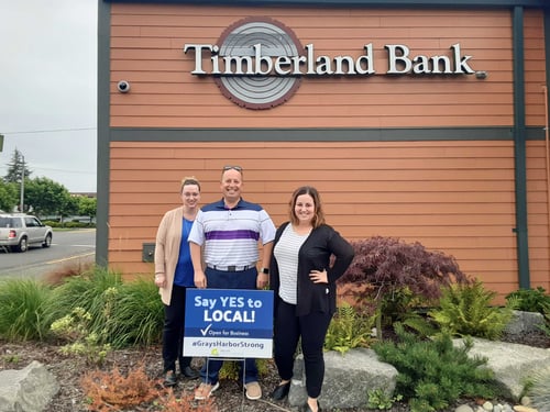 3 Timberland Bank employees pose with a sign reading "Say Yes to Local"
