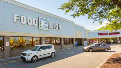 White SUV and tan car driving in front of Food Lion entrance