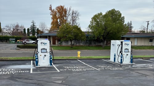 Several EVgo fast-charging units installed in marked parking spaces at a public charging station, with EVgo logos on the chargers, protective bollards around each unit