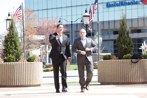 Two personal injury lawyers in suits walking outside a corporate plaza building.