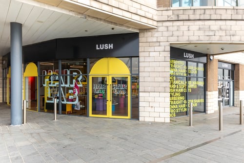 Front entrance to the Hair Lab. Large double doors in bright yellow. Hair Lab in large font printed on window to the left of door. Windows to the right covered in text.