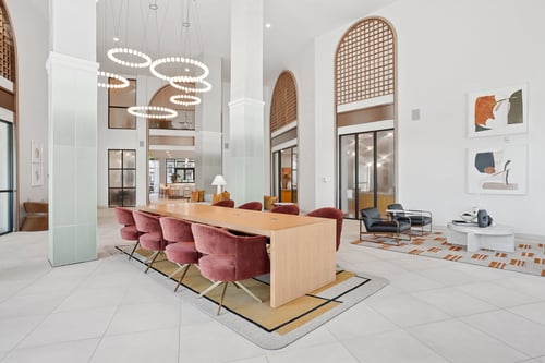 Lobby with double-height ceiling, arched windows, modern circulate chandeliers, and red velvet chairs at a long wooden table.