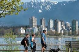 a family walking by the water with a dog. Vancouver city landscape in the back along with mountains.
