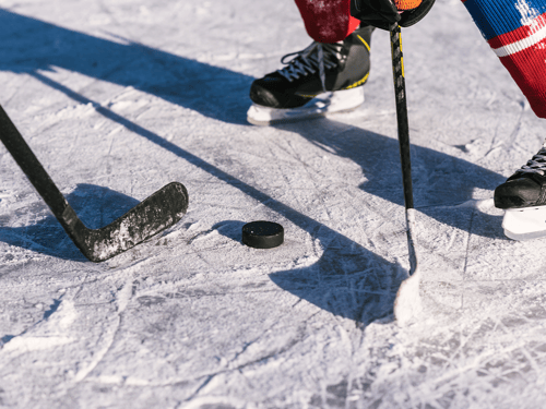 A close-up shot of two hockey sticks and a puck positioned at face-off.