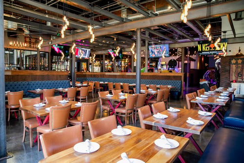 The Americana décor and open-air concept showcases an expansive dining room with large garage door walls leading out to several patio areas equipped with shuffleboard and cornhole.