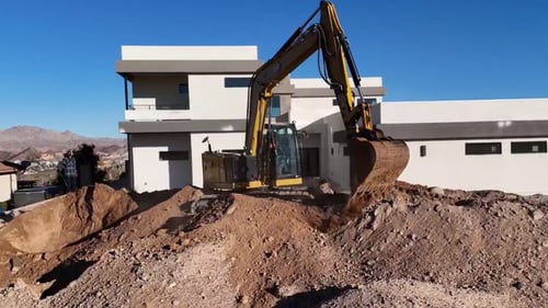 Backhoe moving dirt in front of large modern house