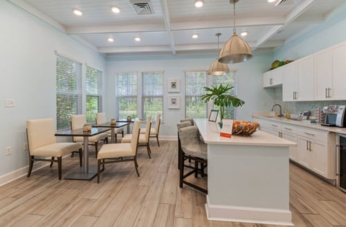 The resident café and social lounge at The Sanctuary at 331 in Santa Rosa Beach, FL, provides a beverage bar, kitchen island seating, and comfortable dining tables in a bright, coastal setting.