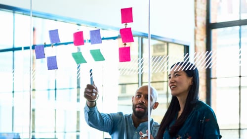 Two colleagues collaborating to map a strategy on the wall
