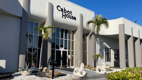 Storefront of Cabot House Furniture Lantana location showing entryway with large windows and palm trees.