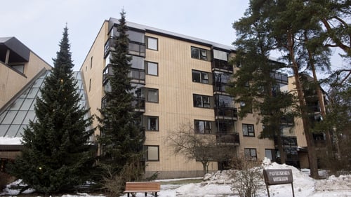 Ulkokuva Kotikalliosta. Rakennus on keltatiilinen. Pihapiirissä on havupuita ja maassa on lunta.