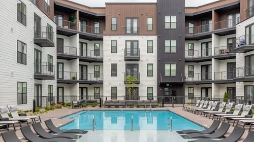 A swimming pool surrounded by lounge chairs in front of apartment buildings at Vintage Edge Nashville Apartments, Nashville