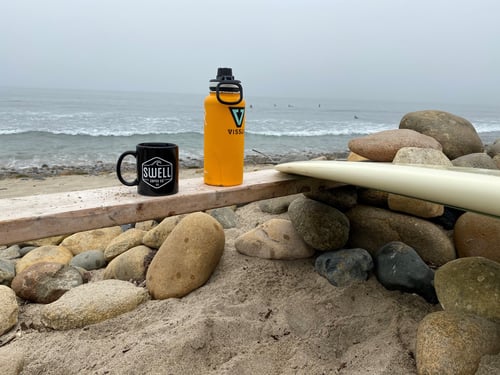 Black coffee mug and yellow water bottle on table by ocean